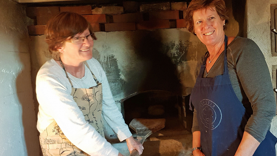 Grete Hjortenberg Paulsen og Wenche Torsøe foran bakerovnen på Basberg Bakstedamer i bryggerhuset
