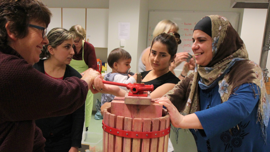 Samling rundt eplepressa: Ghazala Ibrahim og Awaz Hamed fra Syria, og Alyaa Makhzumi fra Irak var ivrig ved eplepressa. Det ble mye latter da det etter hvert ble en tung jobb å presse ut safta. Foto: Ragnhild Bakke.