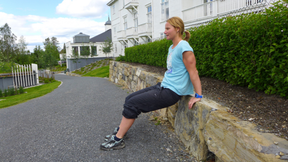 Dips 1 av 2: Støtt deg mot muren med om lag skulderbreit grep. Kroppen er tilnærma strak slik at kun hælane er i bakken. Foto: May-Britt Sægrov. Dips: Støtt deg mot muren med om lag skulderbreit grep. Kroppen er tilnærma strak slik at kun hælane er i bakken. Foto: May-Britt Sægrov.